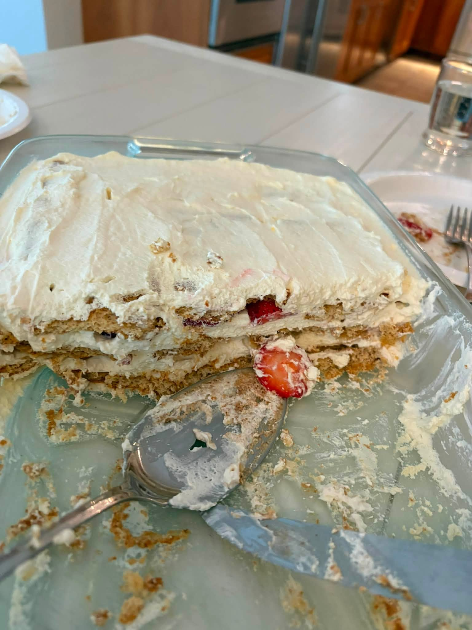 Finished icebox cake cut to show layers of graham crackers, fresh whipped cream, strawberries, and bananas in a glass dish
