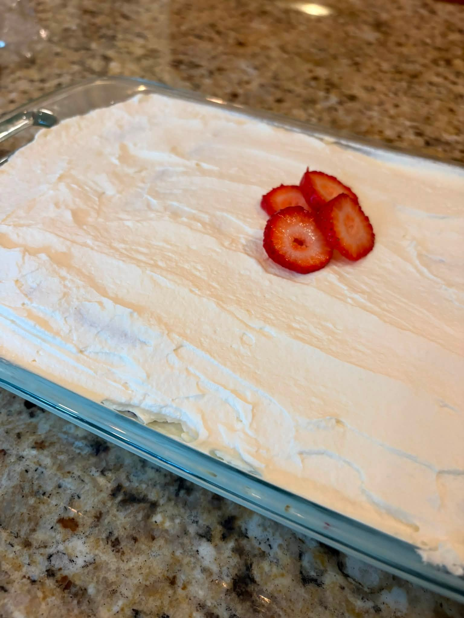 Icebox cake covered with a smooth final layer of fresh whipped cream and garnished with sliced strawberries